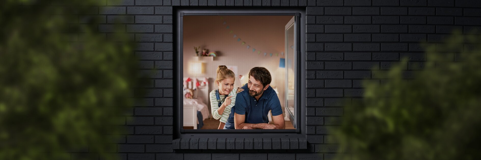 A man and a child are seen through a window, looking into a room decorated with colorful bunting. The building has dark brick walls, and the view is partially framed by blurred greenery. The man is wearing a blue shirt, and the child is sitting beside him. (This text has been generated by AI)