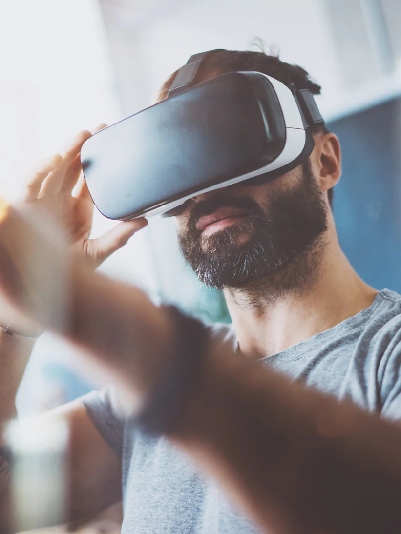 Closeup of bearded young man wearing virtual reality goggles in modern coworking studio. Smartphone using with VR headset. Horizontal, blurred