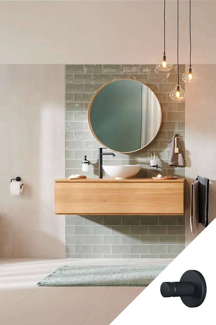 Nowoczesna łazienka ma drewnianą toaletkę z okrągłym lustrem nad nią. Na toaletce znajduje się biała umywalka nablatowa i czarny kran. Zielone płytki tworzą ścianę ochronną. Nad nią wiszą lampy wiszące. Widoczna jest toaleta i wieszak na ręczniki. Czarny wieszak ścienny jest osadzony, zabezpieczony taśmą tesa, co zapewnia czysty i jednolity wygląd, zapewniając stabilność bez wiercenia lub uszkodzenia ścian. (This text has been generated by AI)