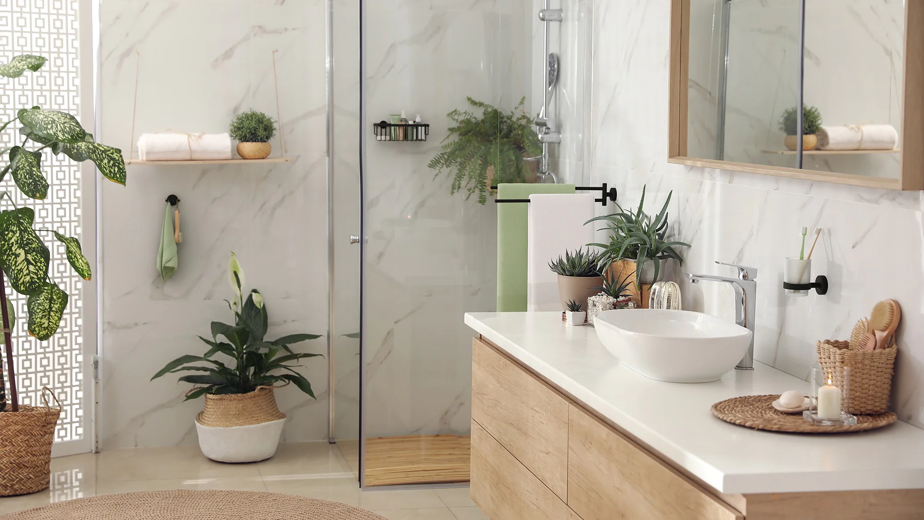 Modern bathroom with a glass shower, wood vanity, and white basin. White marble walls and multiple indoor plants enhance the decor. A mirror hangs above the sink, secured with tesa tape, and there are neatly arranged toiletries on the counter and shelves. (This text has been generated by AI)