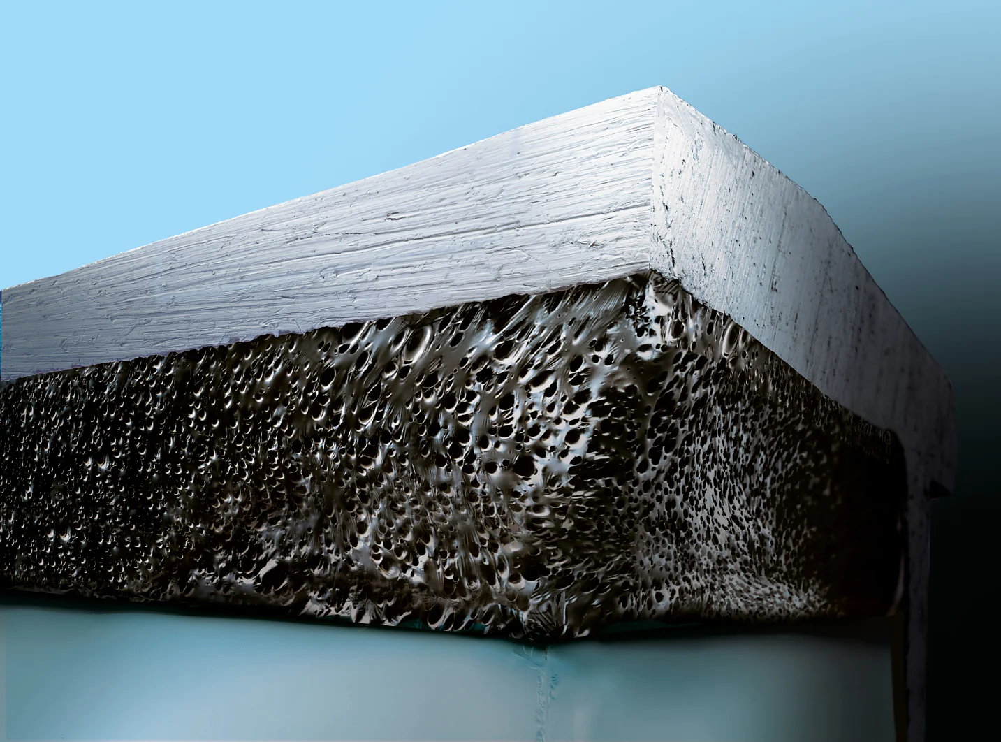 Close-up of a porous, foam-like material layer underneath a smooth, white surface against a gradient blue background. The texture contrasts with the sleek top, highlighting the roughness and openness of the underlying material. (This text has been generated by AI)