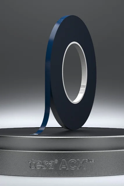 A roll of black adhesive tesa tape is displayed on a round, dark gray base against a gradient gray background. The edge of the tesa tape is slightly lifted. The base features the text VERSA LOOP at the front. (This text has been generated by AI)