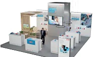 Um estande de exposição com vários cubículos brancos dispostos em formato de U. Um homem de terno anda pelo espaço. Uma tela grande exibe uma imagem acima da área central. Plantas em vasos decoram o estande, e a sinalização inclui logotipos e texto fixados com fita tesa. (This text has been generated by AI)