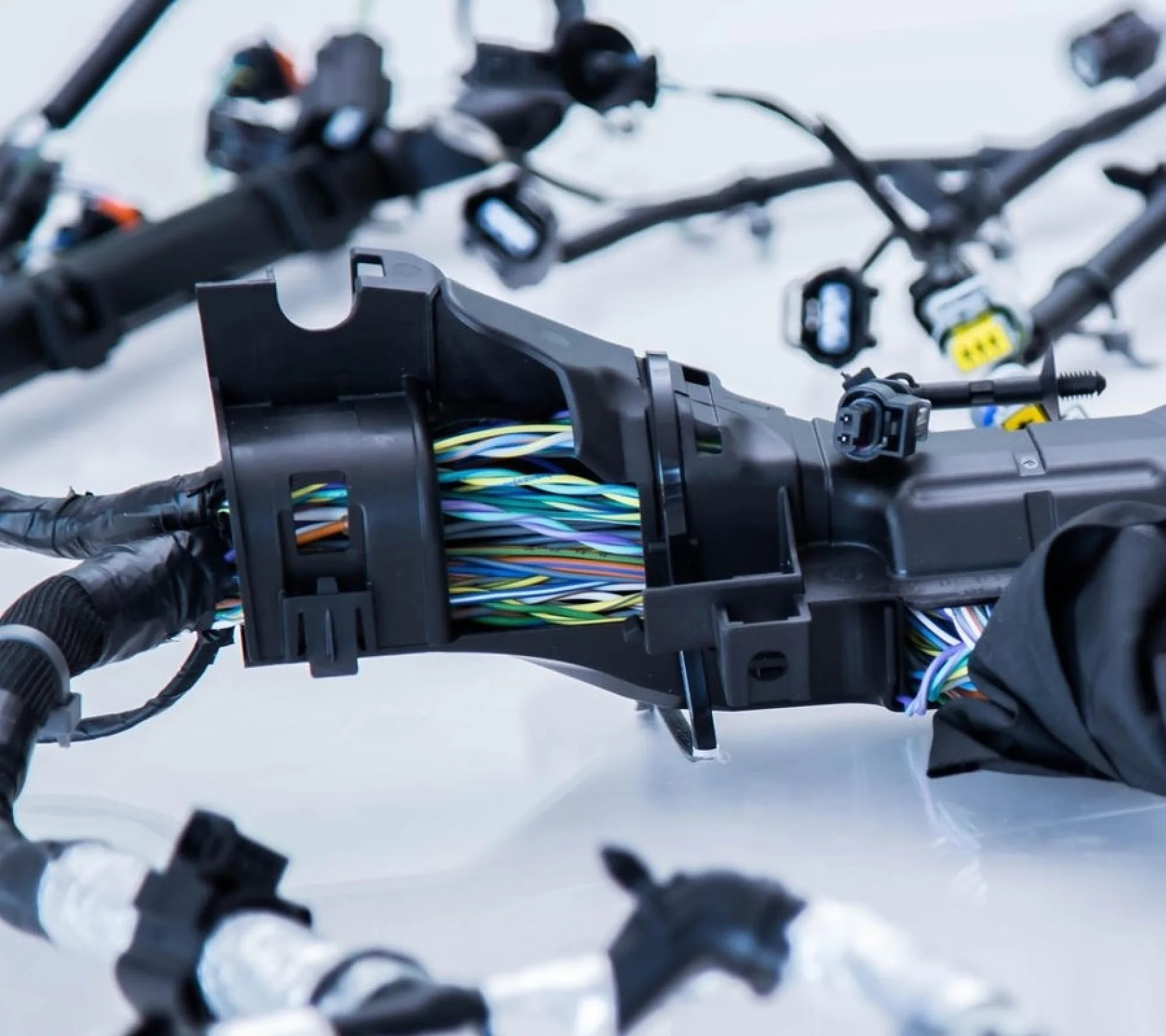 Close-up de um chicote de fiação complexo com vários fios multicoloridos agrupados e conectados com conectores de plástico preto, presos com fita tesa. A configuração repousa sobre uma superfície lisa e de cor clara. (This text has been generated by AI)