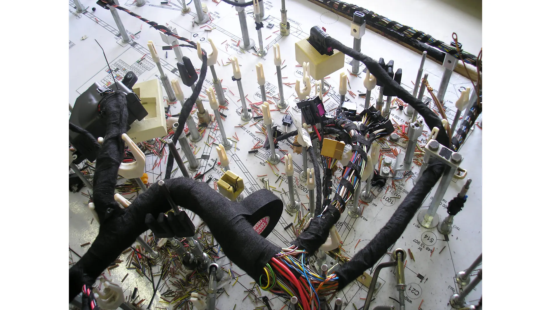 Um complexo chicote de fiação automotiva é montado em uma prancheta; algumas seções de fios são envoltas em fita tesa preta. (This text has been generated by AI)