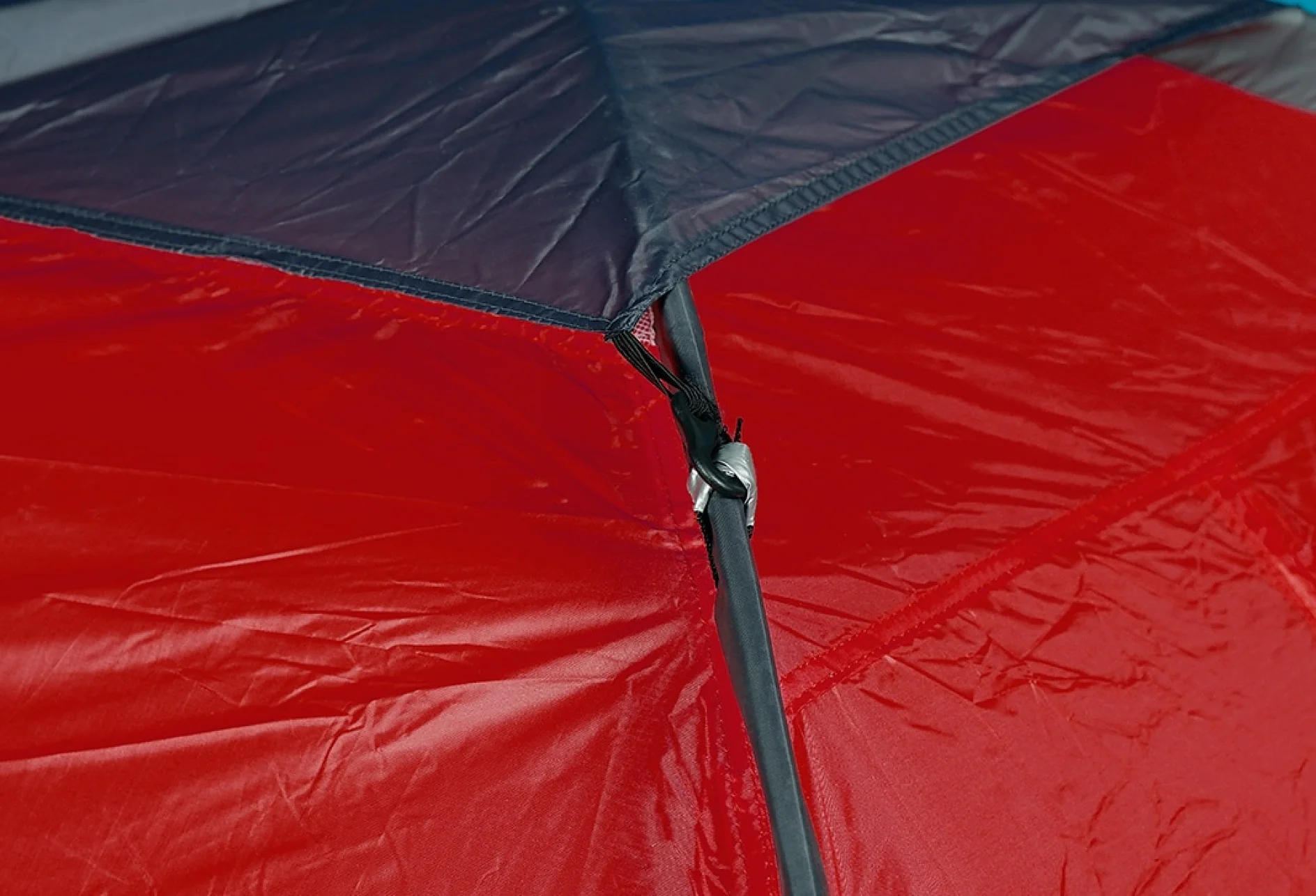 Close-up of the corner of a red and gray tent, showing a black pole connected to the fabric using a plastic joint. The material appears to be waterproof, and light reflections are visible on the surface. (This text has been generated by AI)