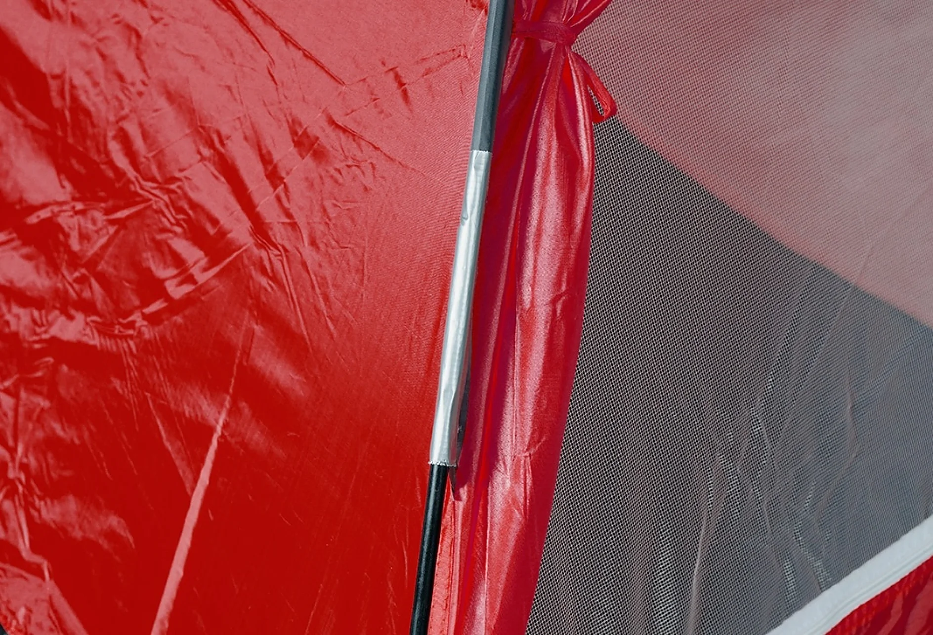 Close-up of a red tent with black and silver poles, showing the intersection where the poles meet the fabric. The tent features a mesh section on one side. The fabric appears taut and evenly stretched, securely fastened with tesa tape. (This text has been generated by AI)