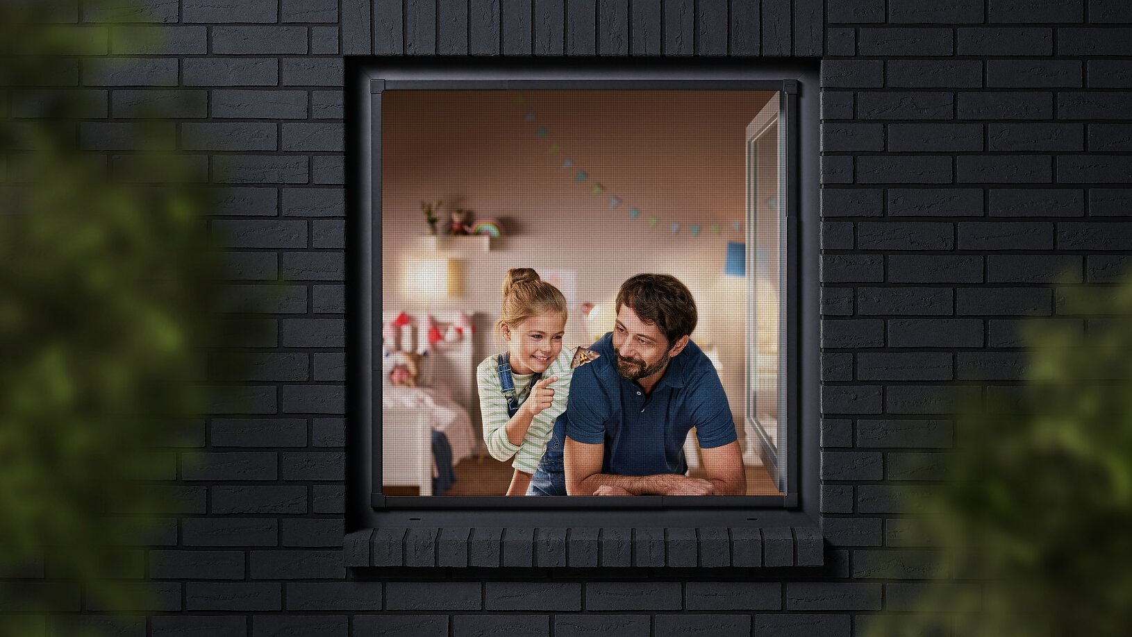 A man and a child are seen through a window, looking into a room decorated with colorful bunting. The building has dark brick walls, and the view is partially framed by blurred greenery. The man is wearing a blue shirt, and the child is sitting beside him. (This text has been generated by AI)
