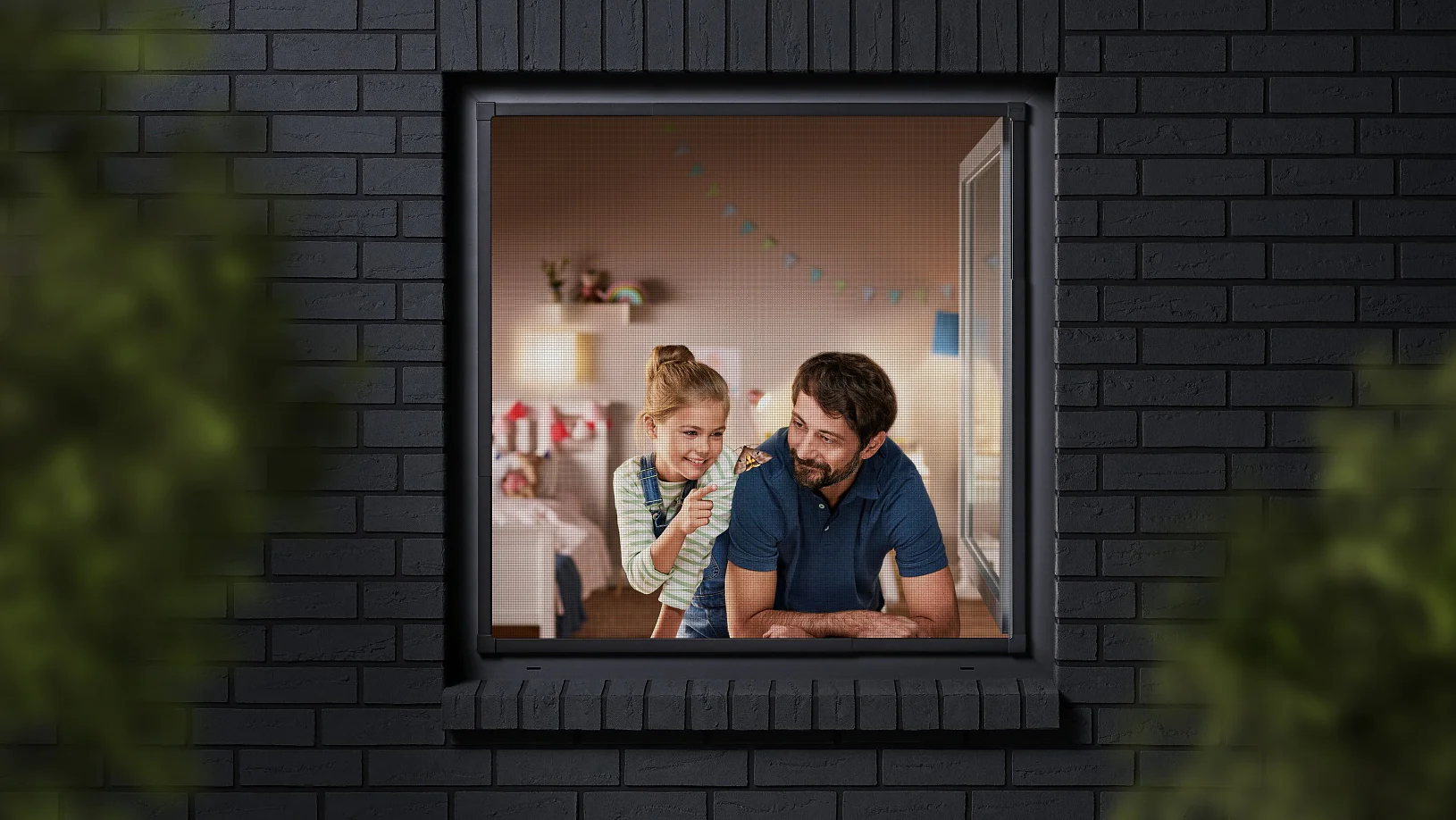 A man and a child are seen through a window, looking into a room decorated with colorful bunting. The building has dark brick walls, and the view is partially framed by blurred greenery. The man is wearing a blue shirt, and the child is sitting beside him. (This text has been generated by AI)