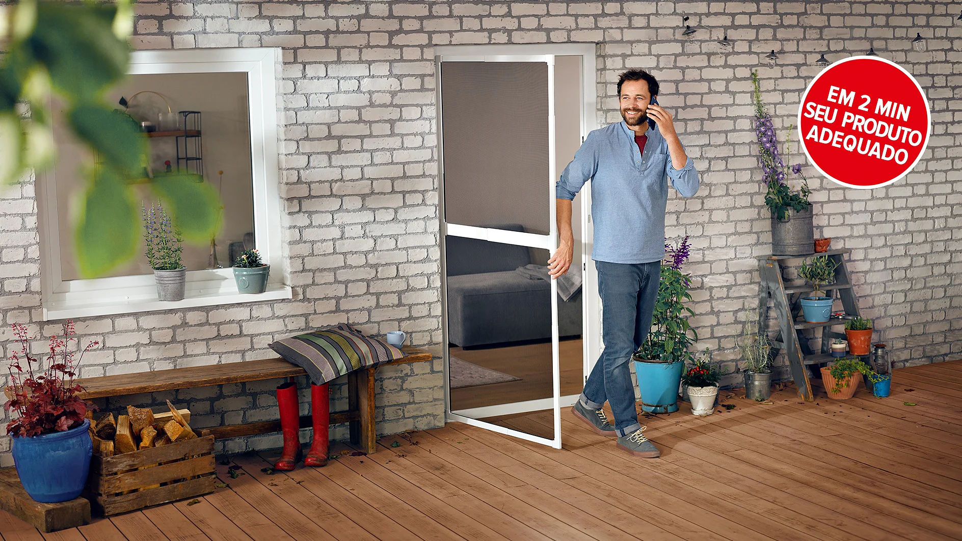Um homem em roupas casuais segura uma porta aberta em uma varanda com um deck de madeira e parede de tijolos brancos. Plantas em vasos e uma pequena escada são visíveis. Uma placa circular vermelha em português é exibida no canto superior direito. (This text has been generated by AI)