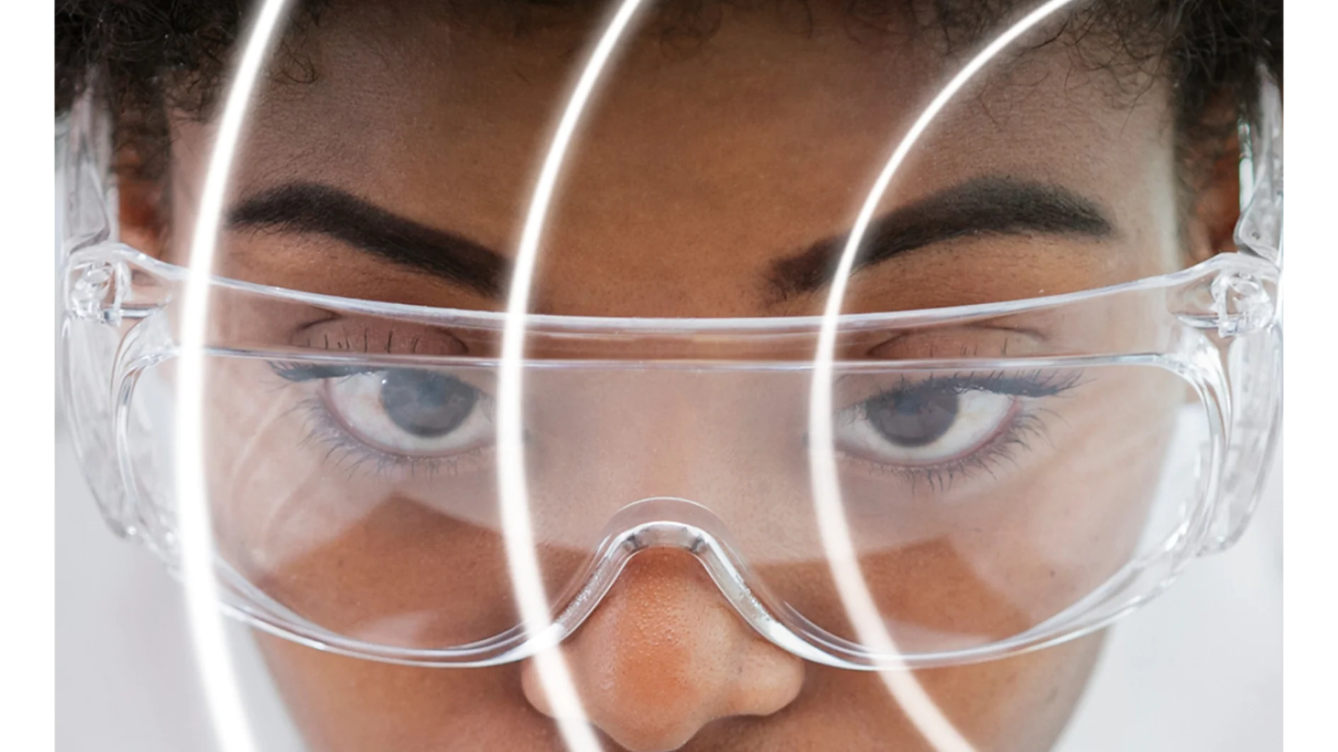 A person wearing clear safety goggles is seen in close-up, with their face partially obscured by concentric circular white lines made of tesa tape. They have short curly hair and a focused expression. The background is white, and the image has a futuristic feel. (Acest text a fost generat de inteligența artificială)