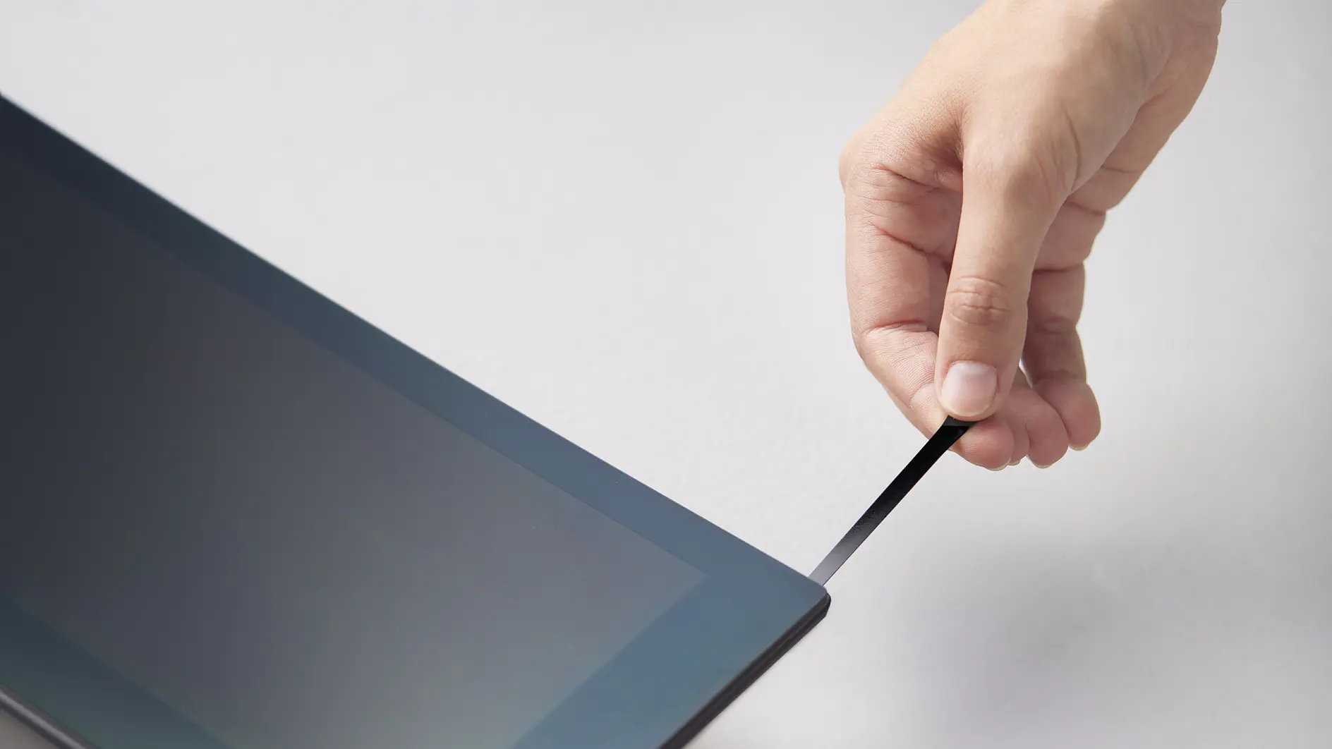 hand pulling black tesa strip from edge of laptop screen in a bright indoor setting (Acest text a fost generat de inteligența artificială)