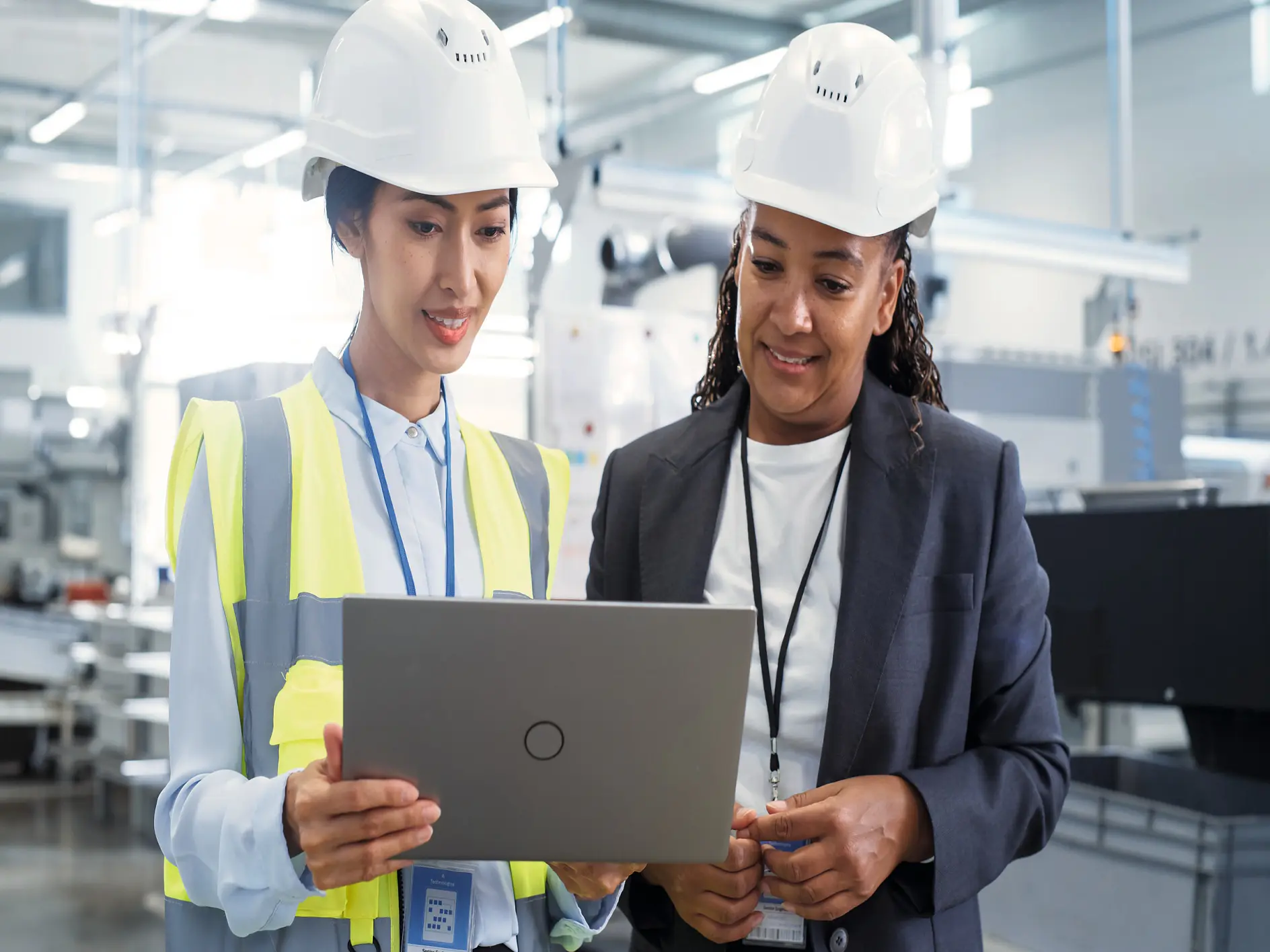 Two professionals in a modern industrial setting looking on a laptop, one wearing a safety vest and hard hat, the other in business attire. (Acest text a fost generat de inteligența artificială)