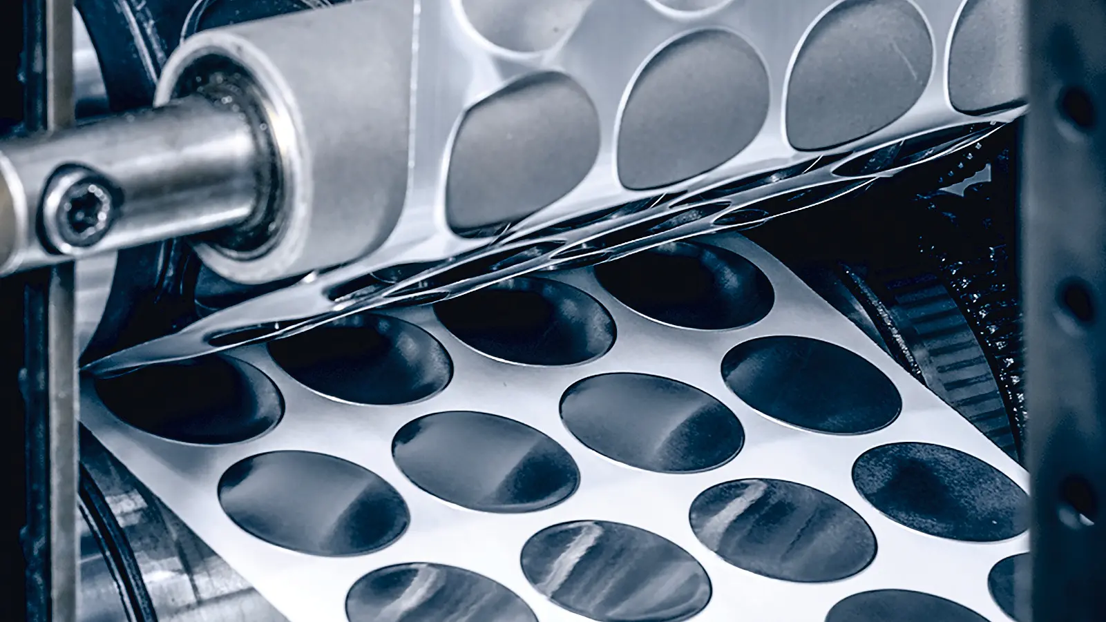 A machine with rollers processes sheets of adhesive paper, cutting out circular stickers. Several rows of stickers are visible, partially separated from the sheet. The surrounding machinery is metallic, with visible gears and supports showcasing tesa tape in action. (Acest text a fost generat de inteligența artificială)