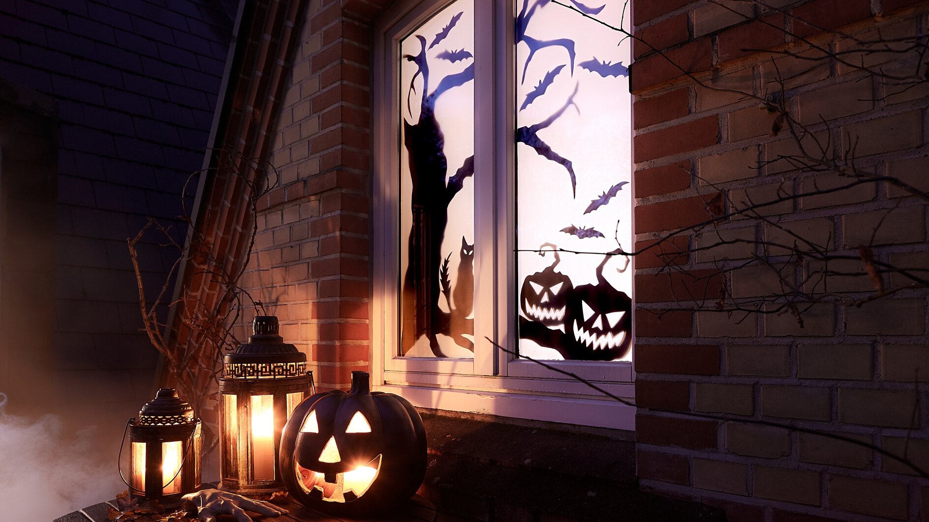En halloween-scen med lysande pumpor och lyktor på en fönsterbräda. Fönstret visar silhuetter av en katt, fladdermöss och träd. Scenen är placerad mot en tegelvägg med torra grenar, och det råder en dimmig stämning. (This text has been generated by AI)
