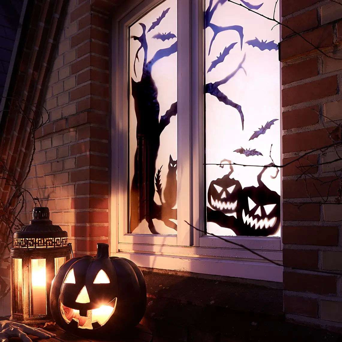 En halloween-scen med lysande pumpor och lyktor på en fönsterbräda. Fönstret visar silhuetter av en katt, fladdermöss och träd. Scenen är placerad mot en tegelvägg med torra grenar, och det råder en dimmig stämning. (This text has been generated by AI)