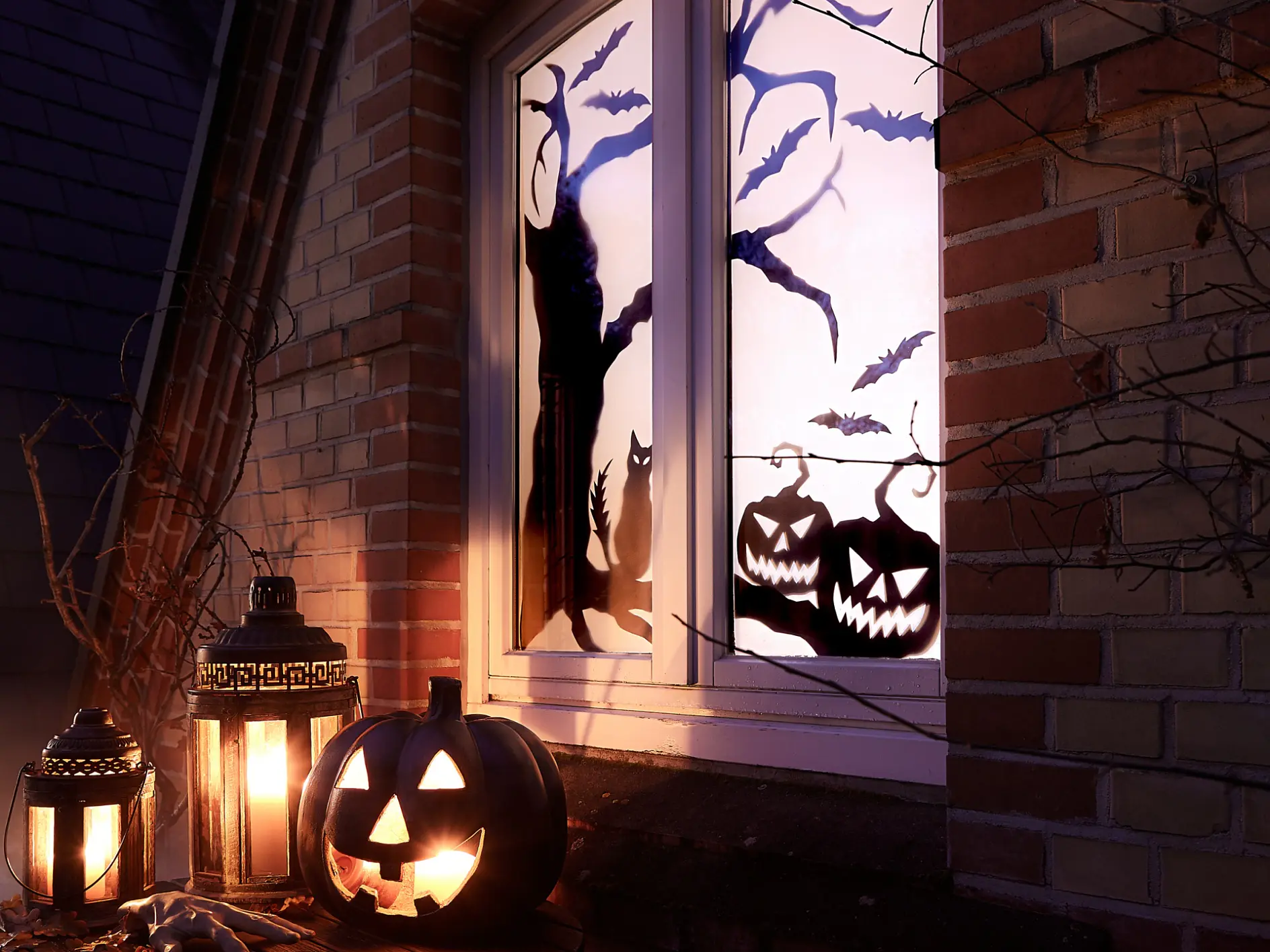 En halloween-scen med lysande pumpor och lyktor på en fönsterbräda. Fönstret visar silhuetter av en katt, fladdermöss och träd. Scenen är placerad mot en tegelvägg med torra grenar, och det råder en dimmig stämning. (This text has been generated by AI)