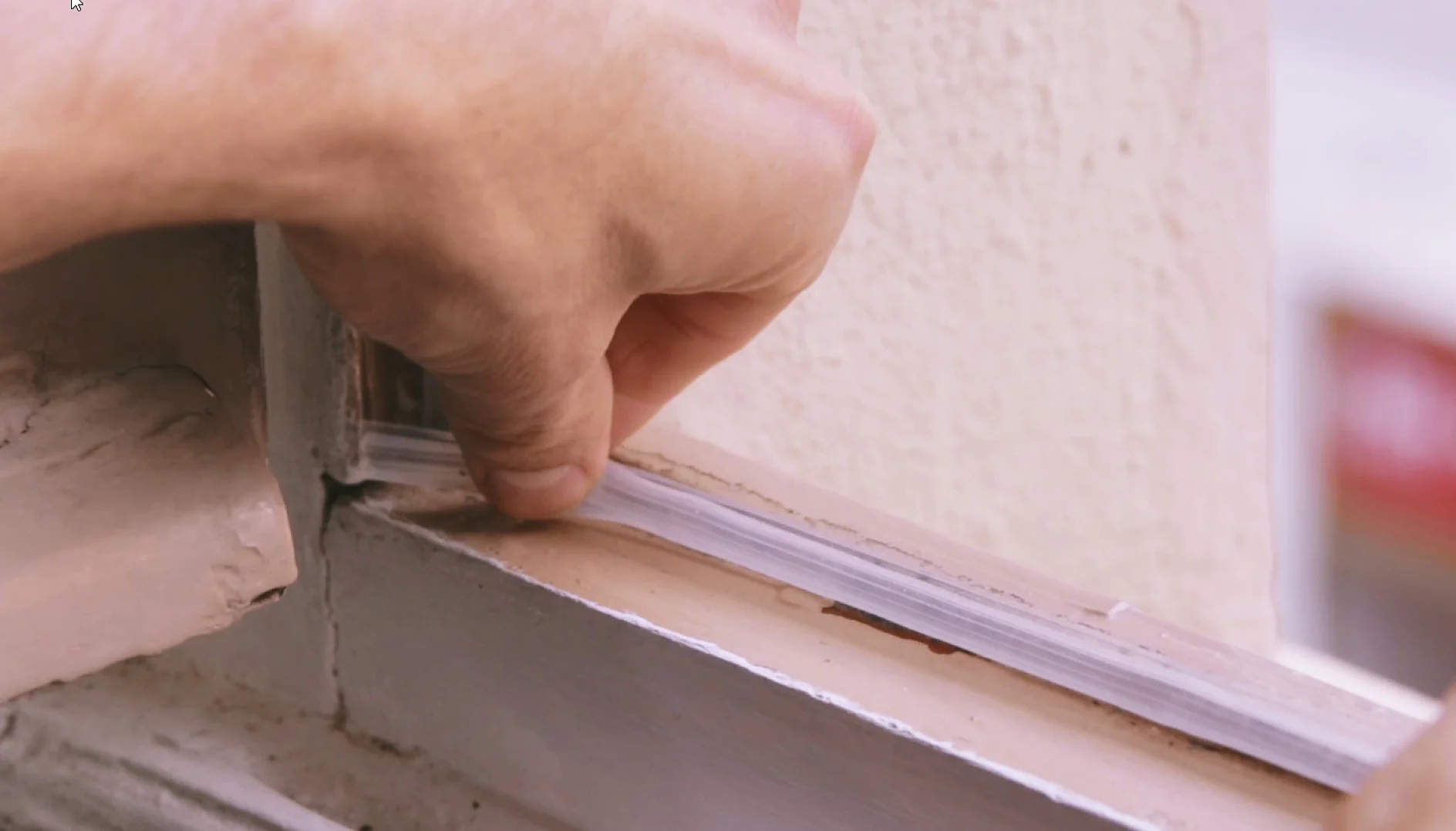 Hand som monterar en tätningslist på ett fönster för att förhindra drag och förbättra isoleringen.