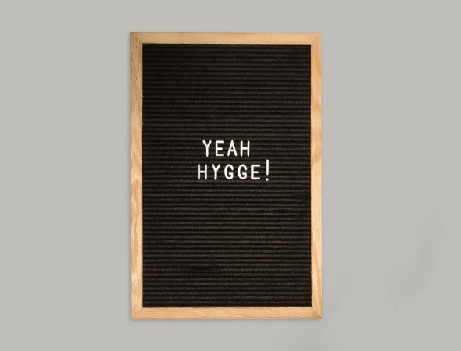 En svart bokstavstavla med en träram visar frasen YEAH HYGGE! med vita versaler, centrerad på en vanlig grå bakgrund. (This text has been generated by AI)