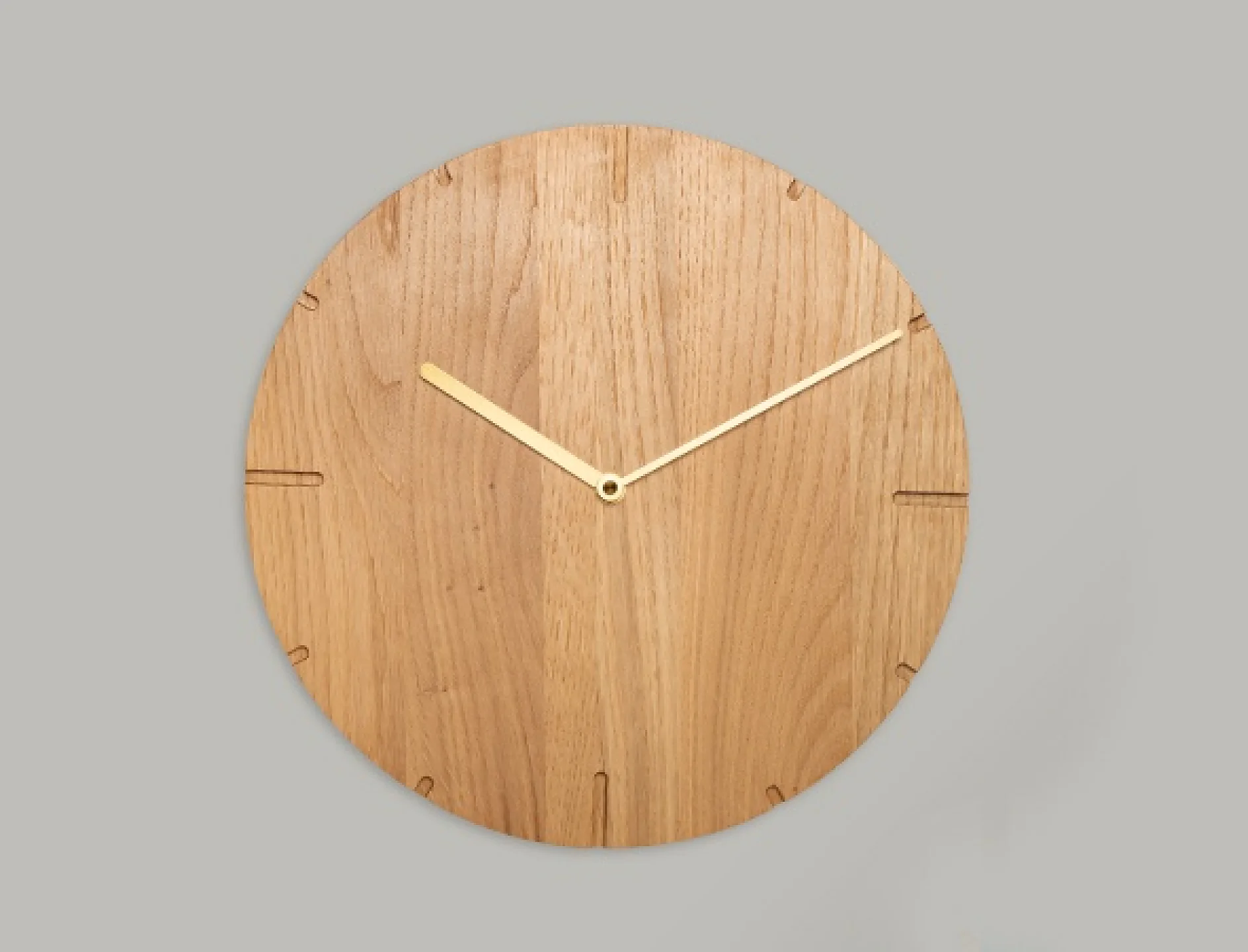 En rund träklocka med minimalistisk design mot en enkel bakgrund. Klockan har guld tim- och minutvisare, med enkla graverade markörer för timpositioner, men inga siffror finns. (This text has been generated by AI)