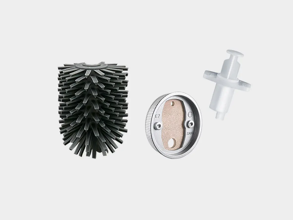 A black round brush head with bristles, a circular metallic component with holes marked E7 and Z06, and a white plastic attachment against a plain background. (This text has been generated by AI)