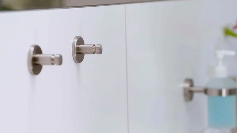 Närbild av badrums- eller köksvägg med metallhållare för handduk eller papper till vänster, tvålpump med blå vätska och blommor till höger samt röd 'tesa'-logotyp i det övre högra hörnet – hygien- och inredningstillbehör.