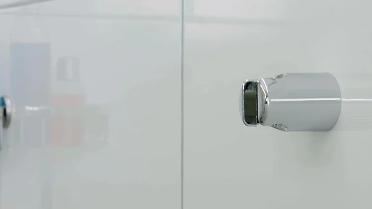 Närbild av en modern dusch med kromat duschmunstycke och väggmonterad hylla med flaskor innehållande blå och orange vätska, mot vita kakelväggar – badrumsinredning, hygienprodukter, duschdesign.