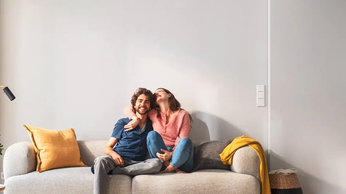 Ein Paar sitzt auf dem Sofa. Sie freuen sich, als sich die Bilder wie von selbst aufhängen.