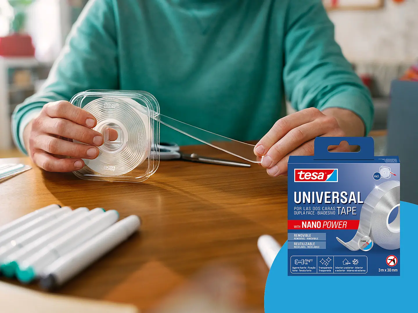 En person använder transparent självhäftande tesa-tejp och drar ut en remsa från rullen. Lådan bredvid visar tesa Universal dubbelsidig tejp med Nano Power-varumärke. Ett vitt föremål och ett blått tyg syns delvis i förgrunden. (This text has been generated by AI)