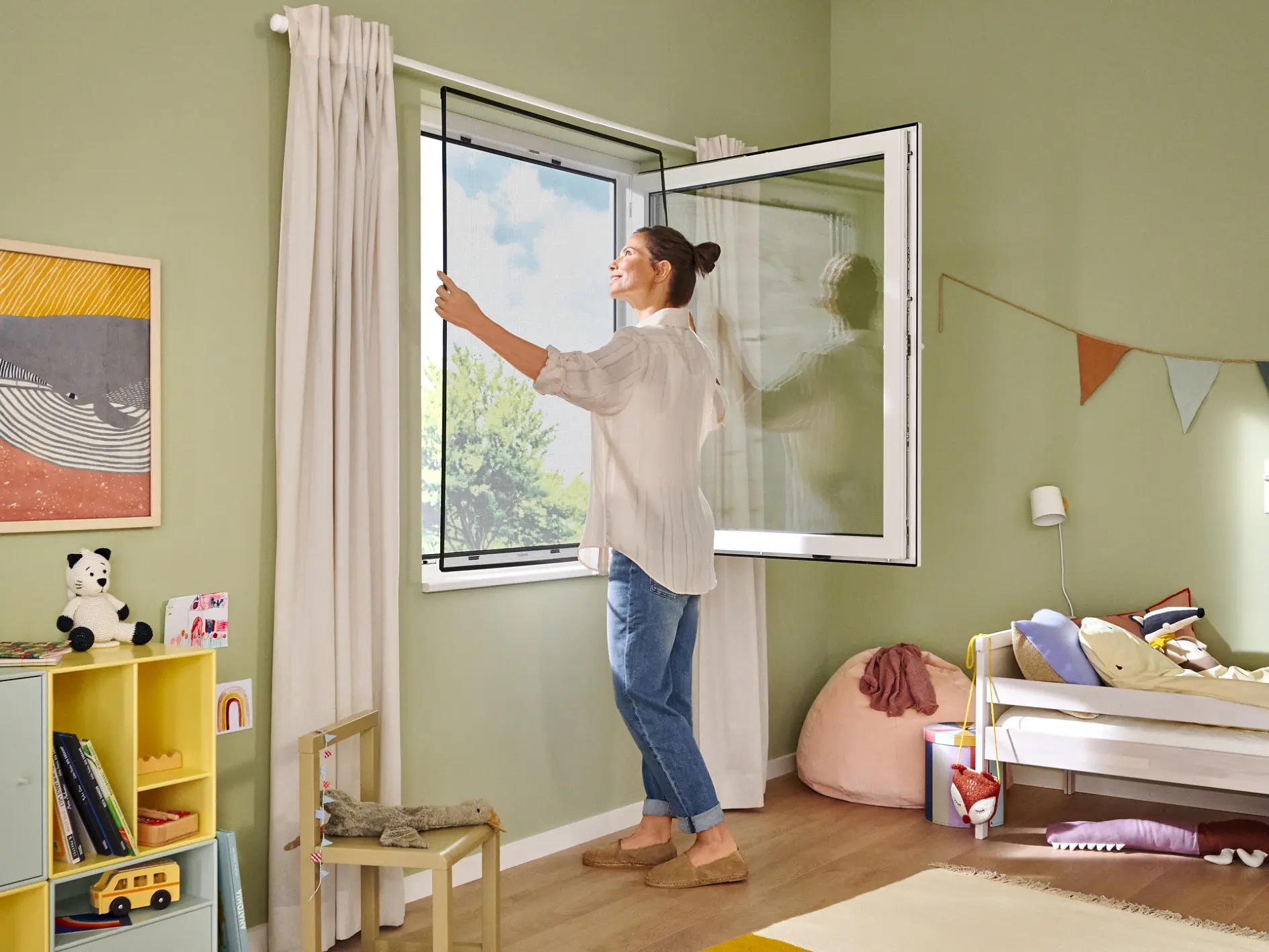 En kvinna öppnar ett fönster i ett barnsovrum med gröna väggar. Rummet har en säng, leksaker och färgglada dekorationer, inklusive en väggbanner fäst med tesa-tejp och inramad konst. En liten hylla håller böcker och en gul leksaksbuss. Naturligt ljus strömmar in. (This text has been generated by AI)