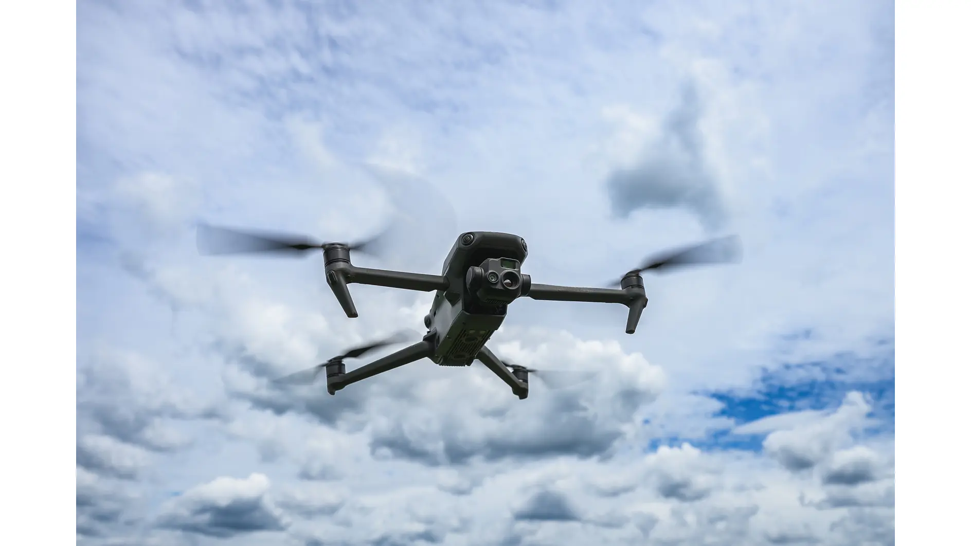 Modern quadcopter-drönare svävar i luften mot en dramatisk molnig himmel. Obemannat luftfartyg med kamera används för fotografering, inspektion, kartläggning och tekniska tillämpningar.
