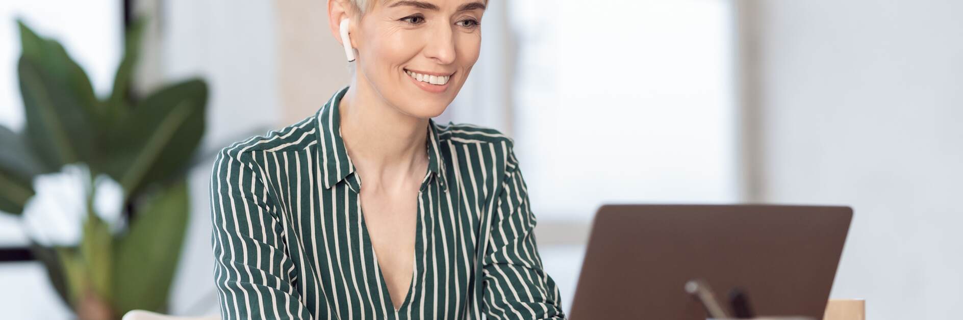 Mature Lady Working On Laptop In Earphones Sitting In Office
