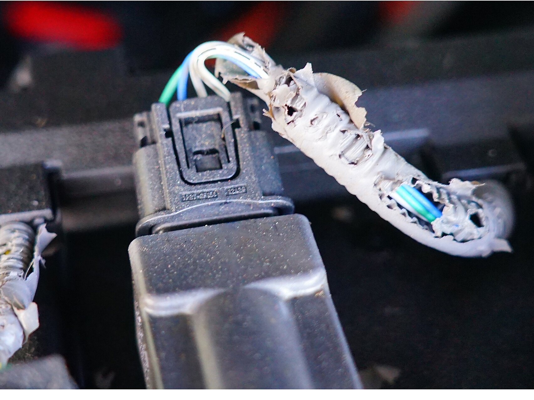 Three electrical connectors with visible damage to the insulation, exposing wires. The insulation appears chewed or torn, showing multiple colored wires inside. The connectors are attached to a black base and wrapped with tesa tape for added protection. (This text has been generated by AI)