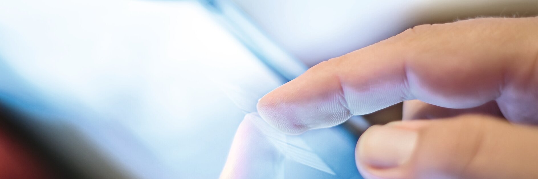 Hand tapping a tablet screen indoors, focusing on the interaction between finger and device display.