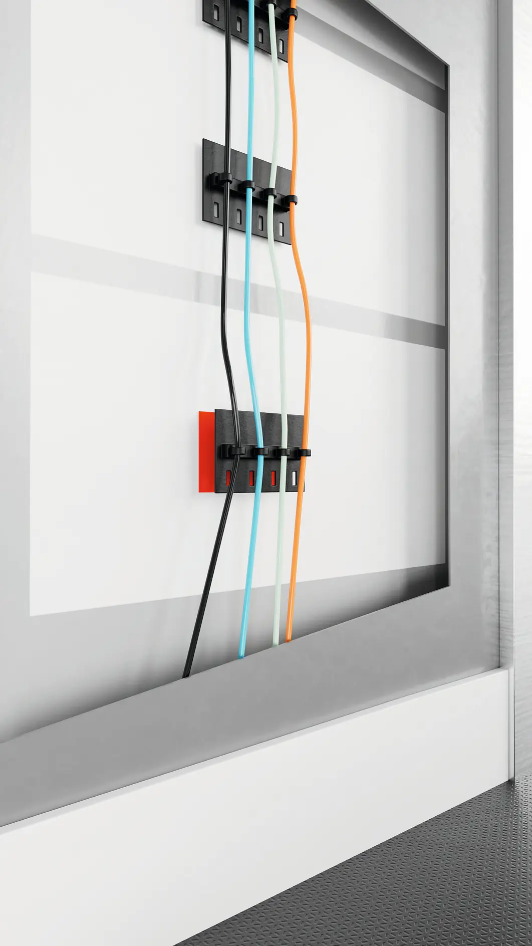 tesa branded black and red cable clips organizing orange, blue, and black cables on a white wall in an indoor setting (This text has been generated by AI)