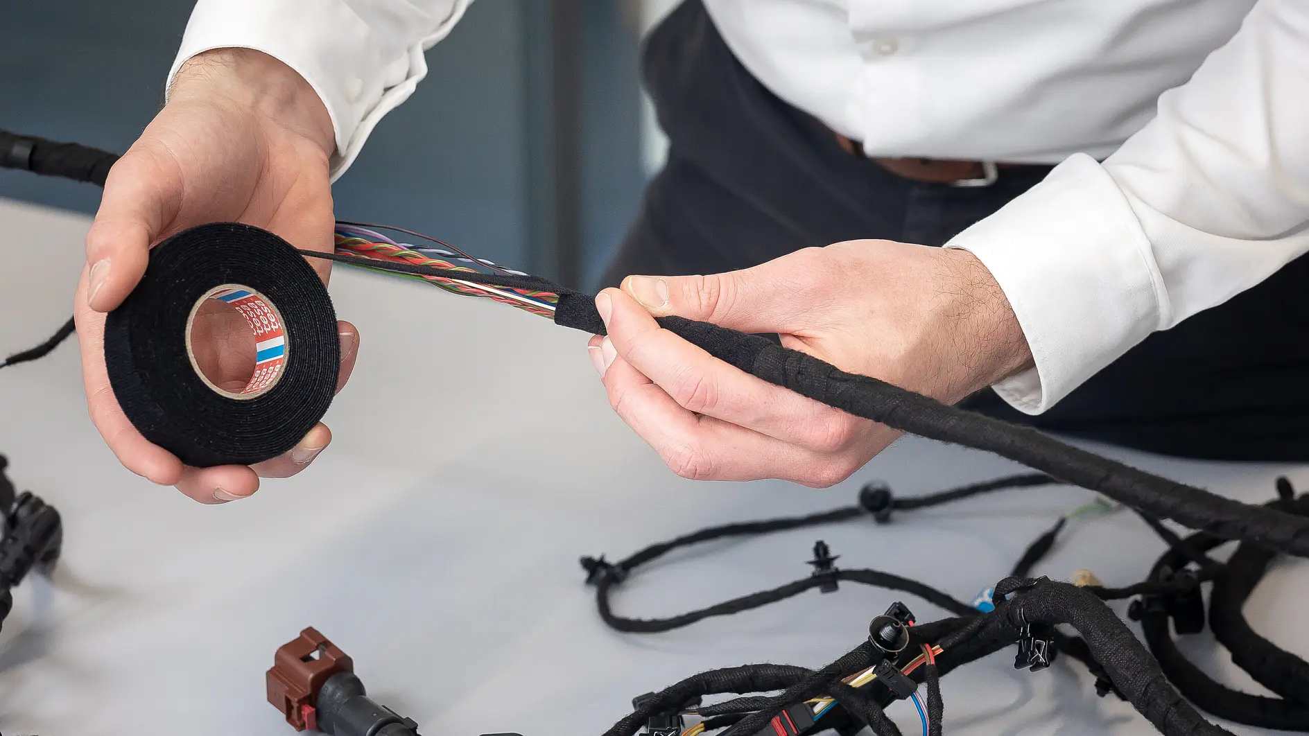 tesa tape being applied to an automotive wiring harness on a white table in an indoor workshop setting