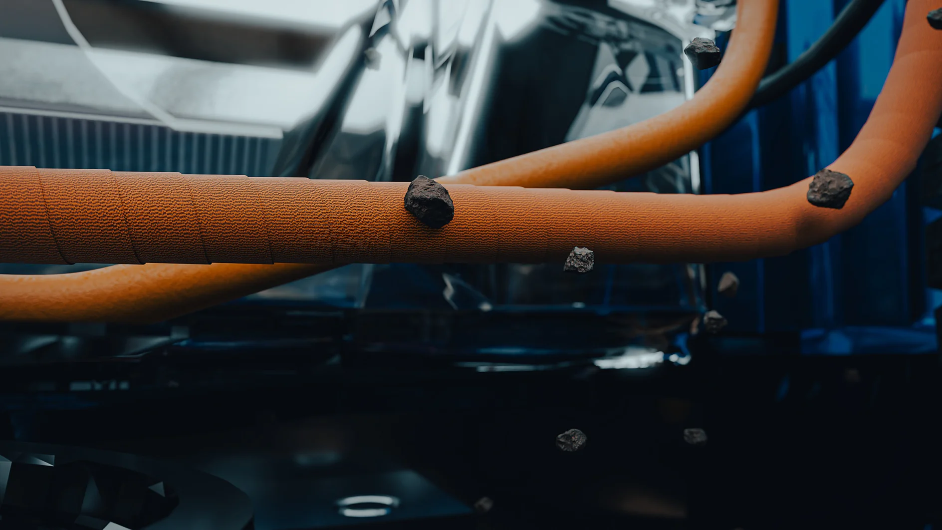 Close-up of two orange tubes with a tesa tape-like textured surface, intertwined in midair, with debris floating and a metallic blur behind. (This text has been generated by AI)