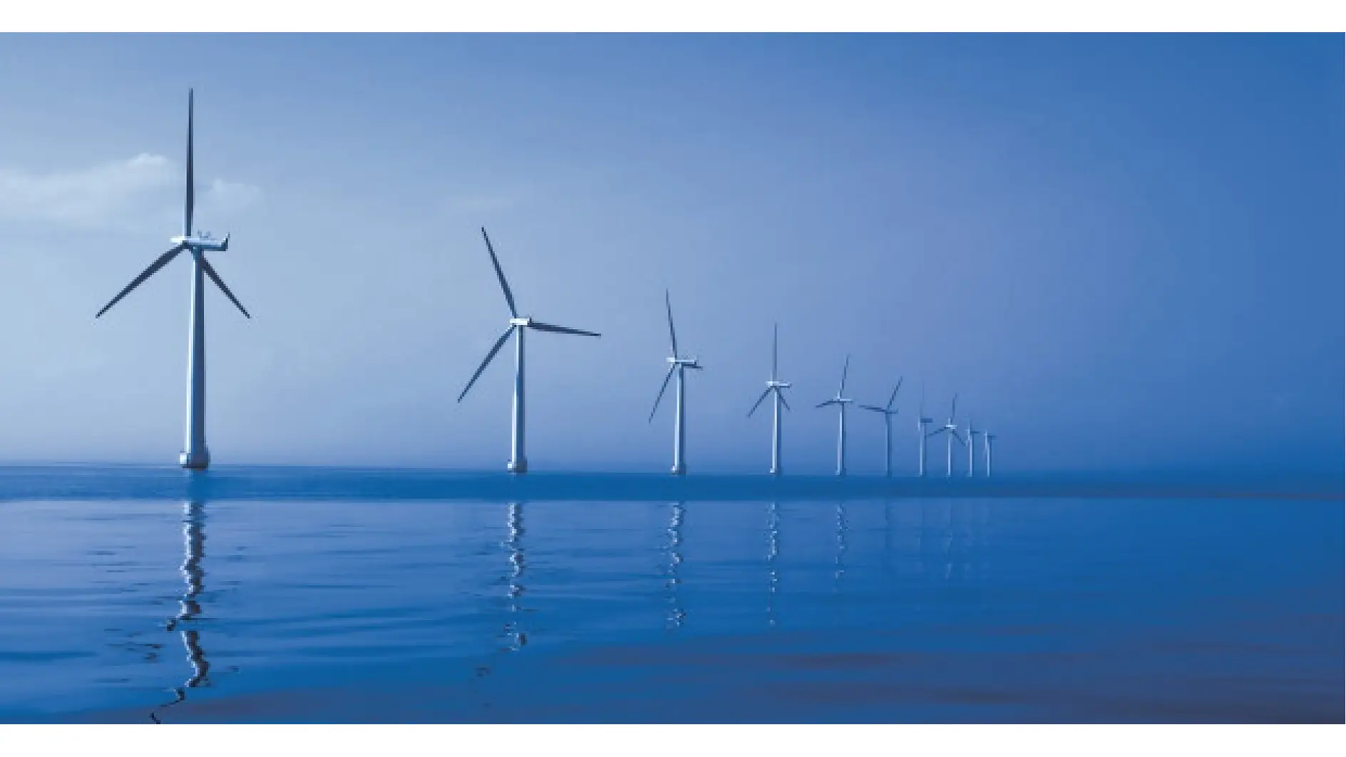 A row of offshore wind turbines stands in the ocean under a blue sky. The turbines are evenly spaced, and their reflections are visible in the calm water. (This text has been generated by AI)