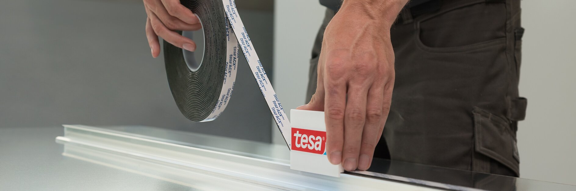 man applying white tesa tape from a roll onto a metal surface indoors, focusing on precise alignment and measurement