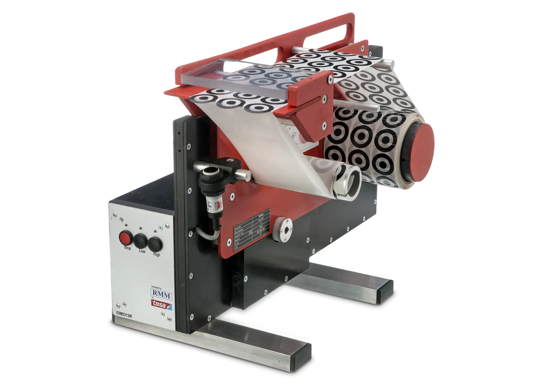 A label applicator machine with a stainless steel frame. It features a roll of circular labels with black and white concentric circles, and control buttons on the side. The machine is designed for applying tesa tape labels to various products.