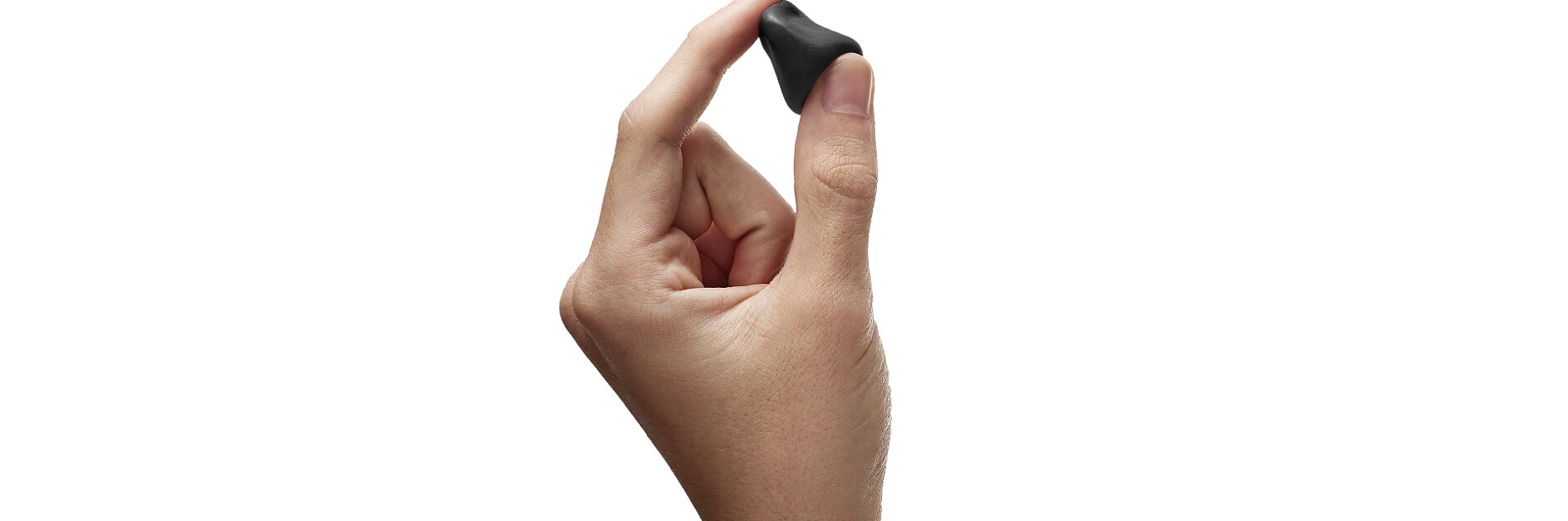 A persons hand is holding a small, black, circular object between the thumb and index finger. The person is wearing a green sleeve. The background is white.