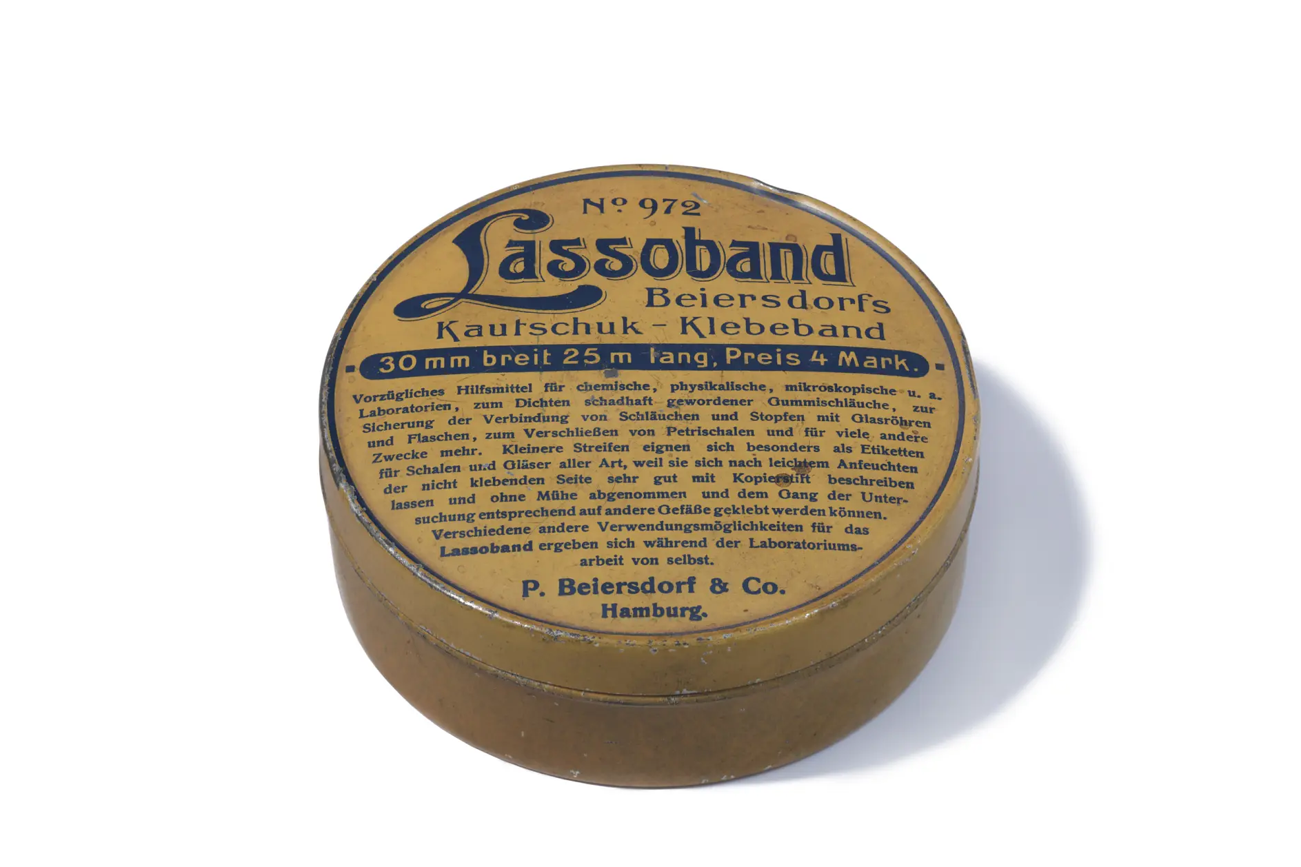 Vintage metal tin labeled Lassoband Beiersdorfs Kautschuk-Klebeband with specifications in German, including dimensions 30 mm breit, 25 m lang. It is associated with P. Beiersdorf & Co., Hamburg. Tan and round in shape, featuring the well-known tesa tape brand.