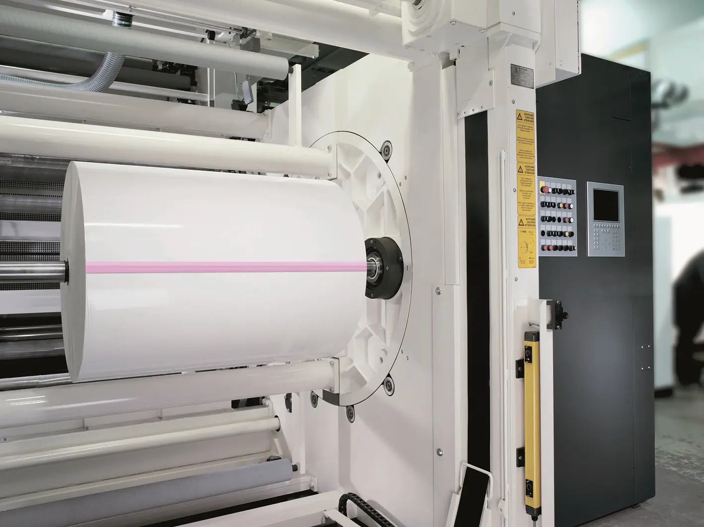 A large industrial printer with a white paper roll mounted on it. The machine has control panels on the side, with buttons and a display screen. The printer features a pink line running across the center of the paper roll thats created using tesa tape. (This text has been generated by AI)