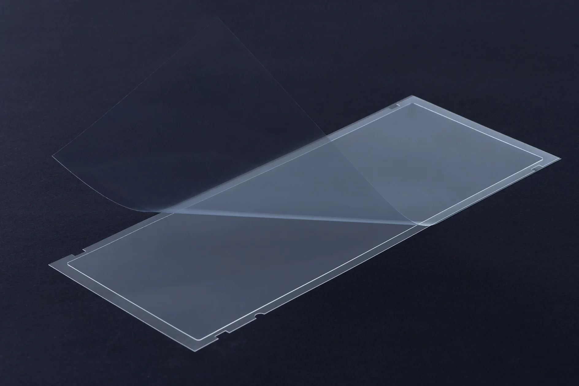 A transparent rectangular sheet or film is partially lifted from a flat, similar-sized base against a dark background using tesa tape. (This text has been generated by AI)