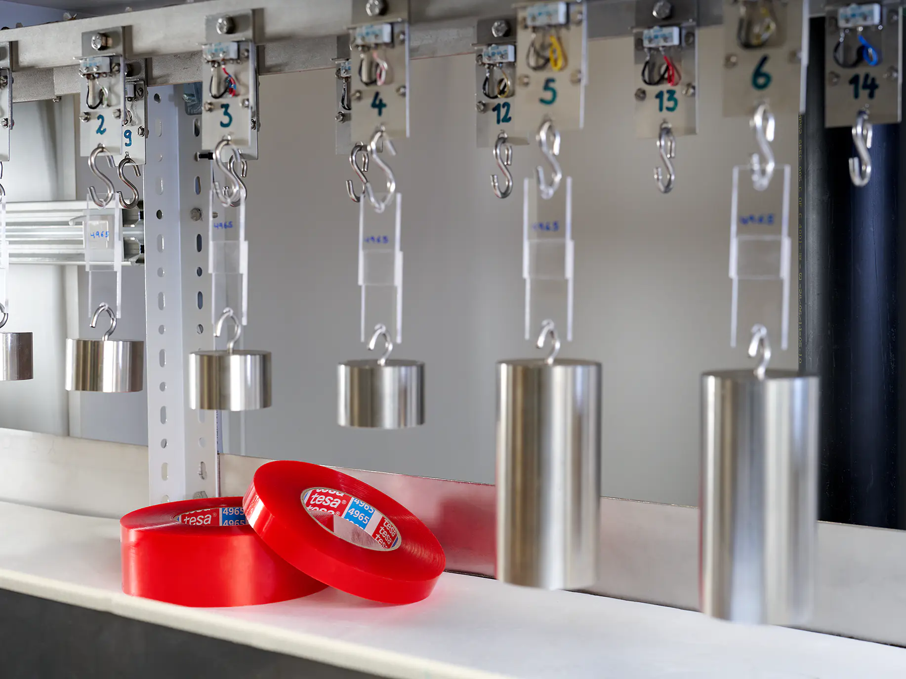 tesa red adhesive tape rolls and metal cylinders hanging from hooks in an industrial indoor setting