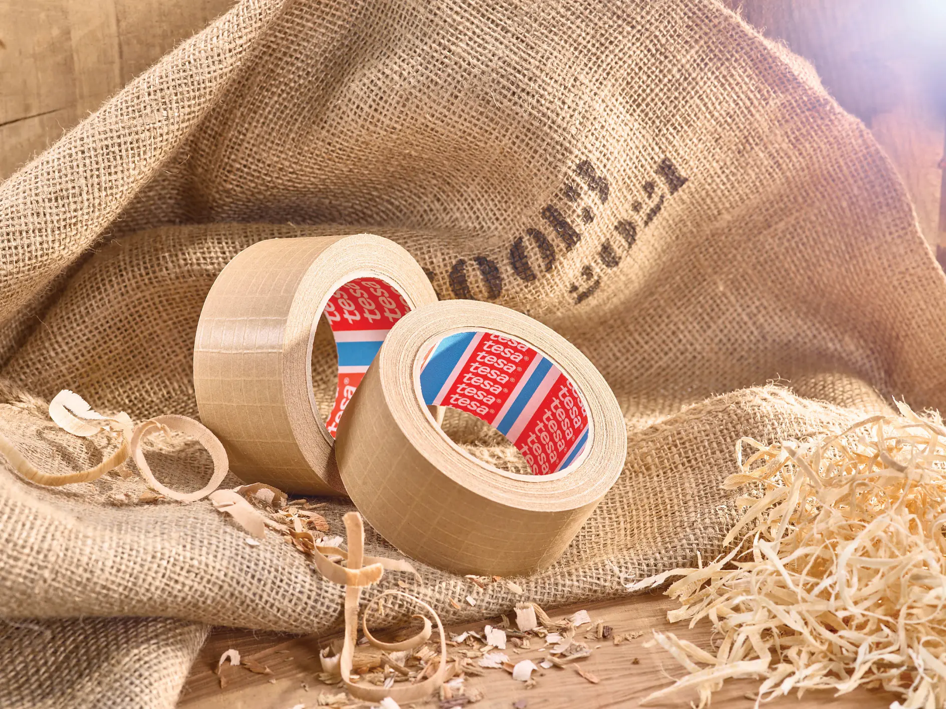 two rolls of tesa adhesive tape on burlap fabric with wood shavings and straw in a rustic indoor setting (This text has been generated by AI)