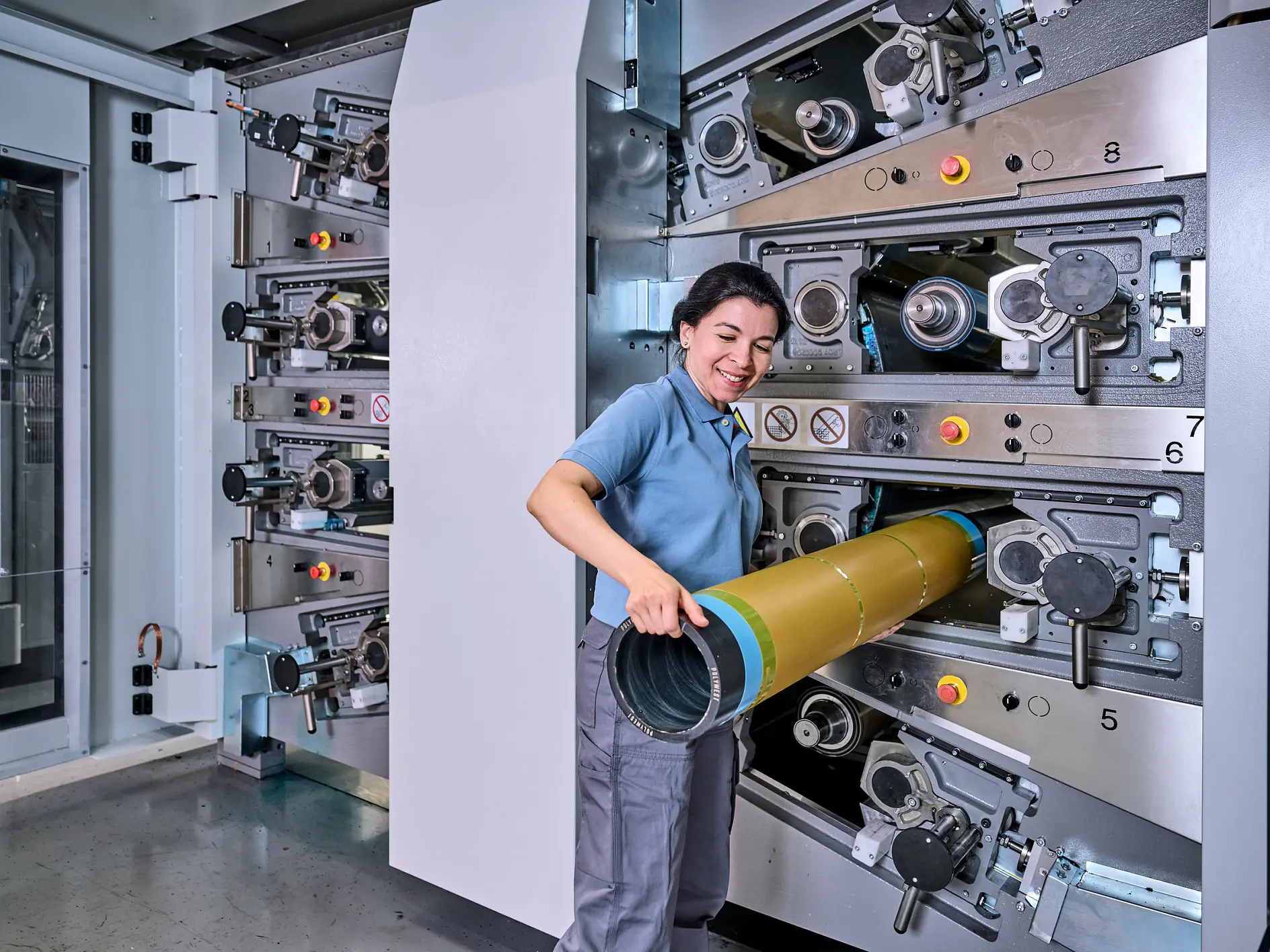 Kapalı alanda büyük endüstriyel baskı makinesini kullanan kadın, fabrika ortamında sarı ruloyu birden fazla ruloya ayarlıyor (This text has been generated by AI)