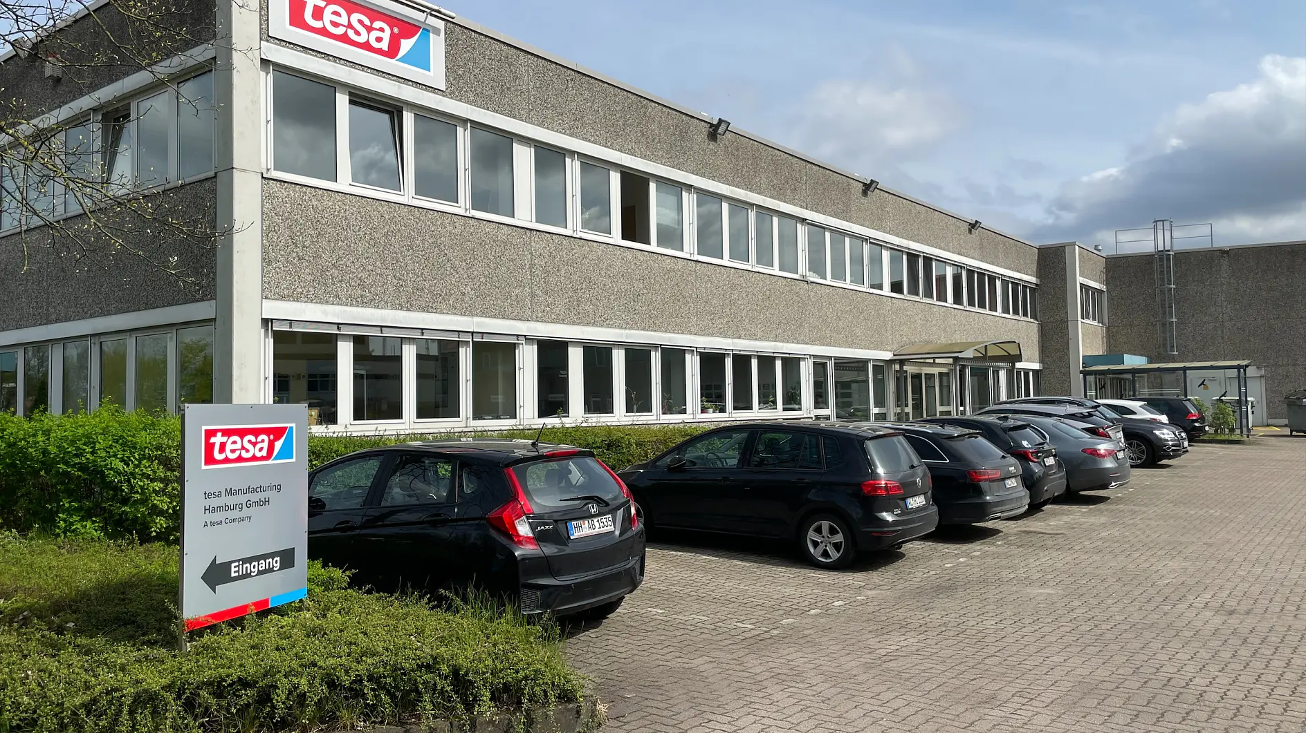 tesa Manufacturing Hamburg binası, önünde park etmiş arabalar ve girişte yönlendirme tabelası