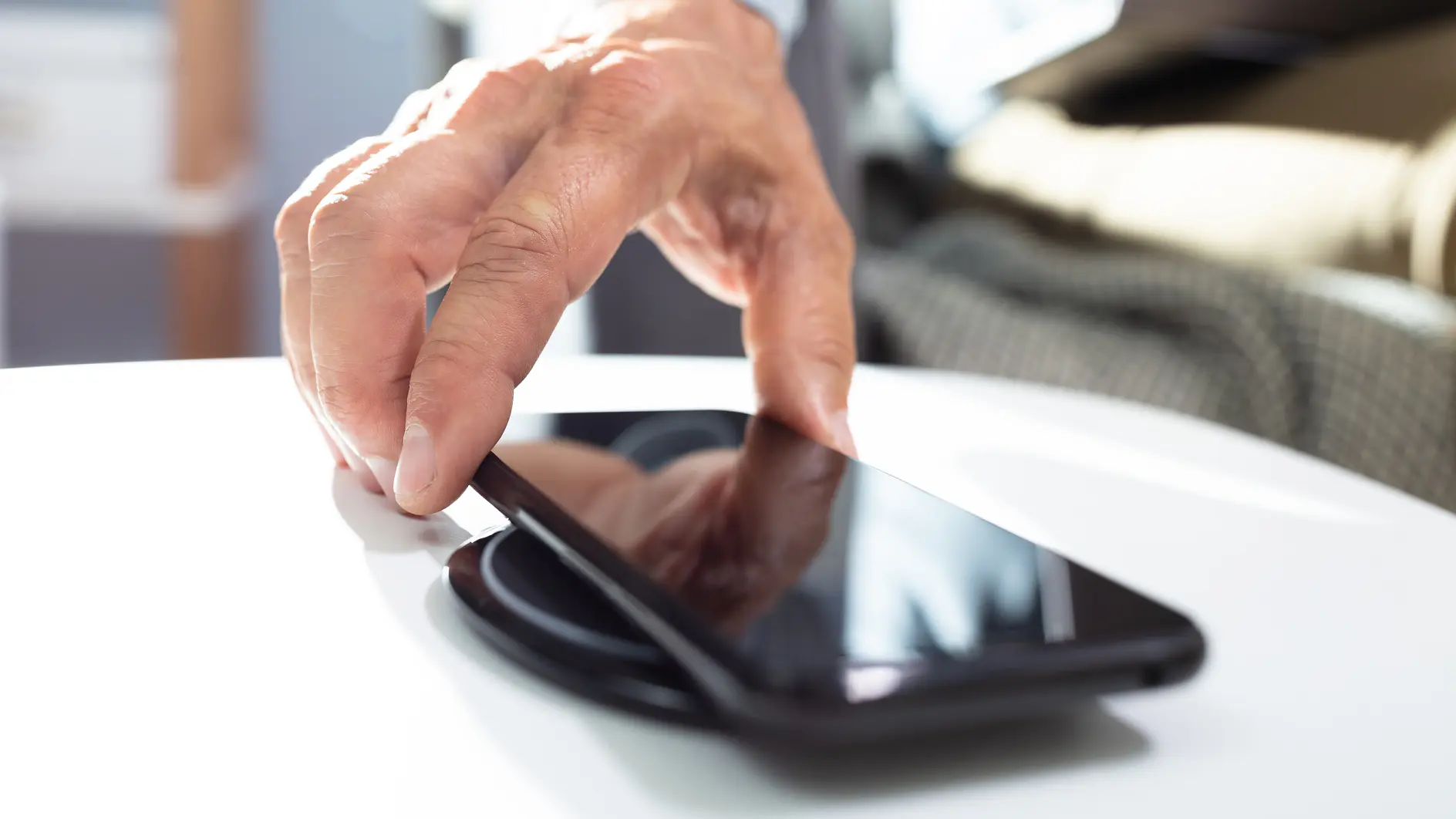 hand placing a black smartphone on a white table in a bright indoor setting with blurred background tesa