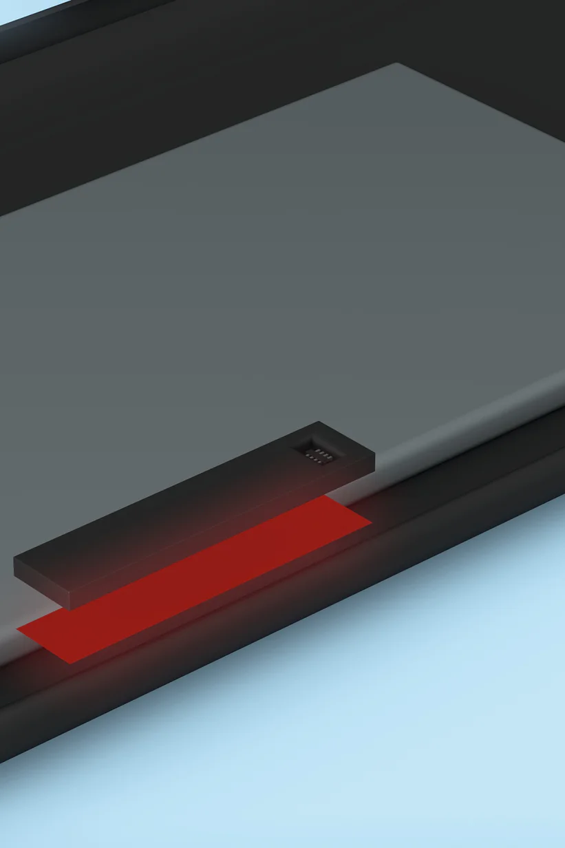 Close-up of a smartphone charger with a rectangular charging pad and a small LED indicator glowing red. The pad is placed on a black surface, likely the back of a phone, against a light blue background. (This text has been generated by AI)